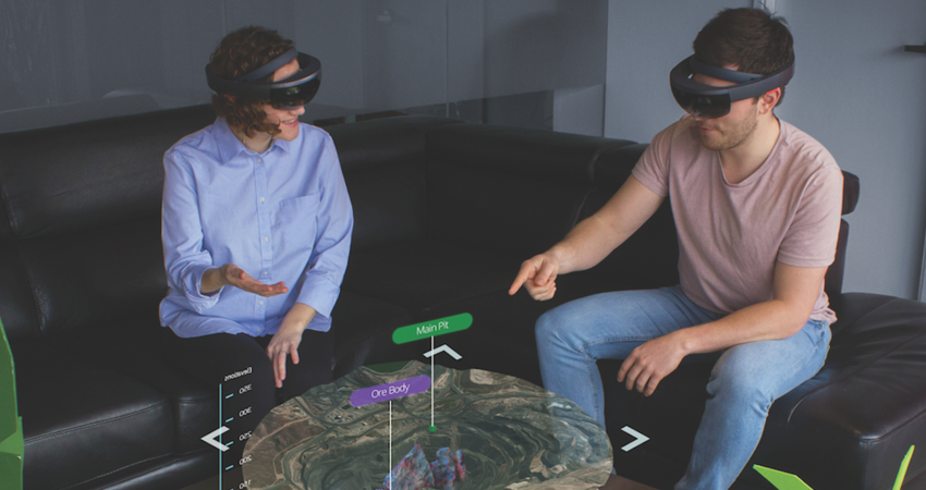 Two people wearing AR headsets interact with a 3D holographic map on a table.